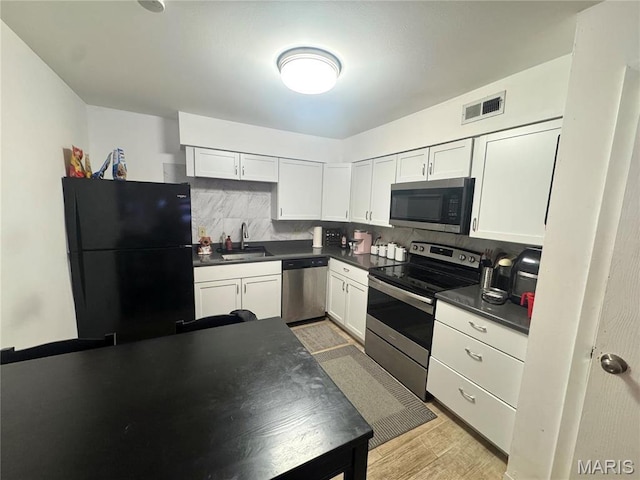 kitchen with appliances with stainless steel finishes, dark countertops, a sink, tasteful backsplash, and white cabinetry