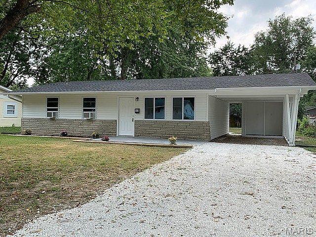ranch-style home featuring gravel driveway, a front lawn, a carport, and stone siding
