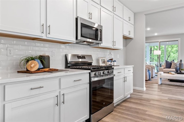 kitchen with appliances with stainless steel finishes, white cabinetry, decorative backsplash, light wood finished floors, and recessed lighting