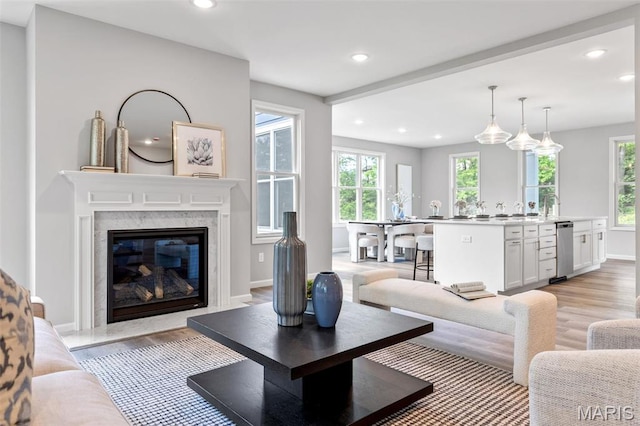 living area featuring light wood-style floors, recessed lighting, healthy amount of natural light, a high end fireplace, and baseboards
