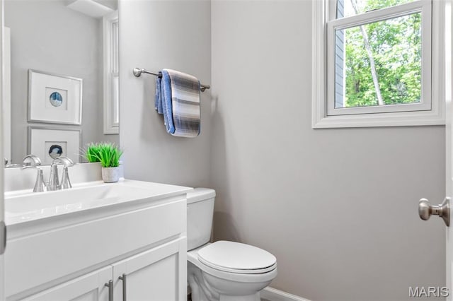 bathroom with healthy amount of natural light, toilet, vanity, and baseboards