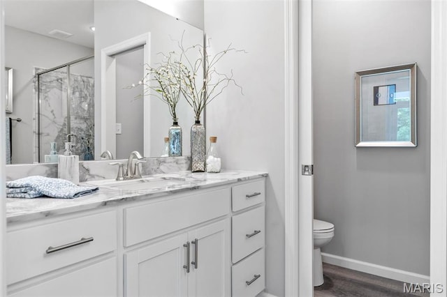 bathroom with a shower stall, toilet, vanity, wood finished floors, and baseboards