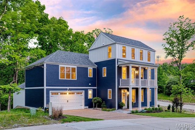 view of front facade featuring covered porch, a balcony, an attached garage, gravel driveway, and a shingled roof
