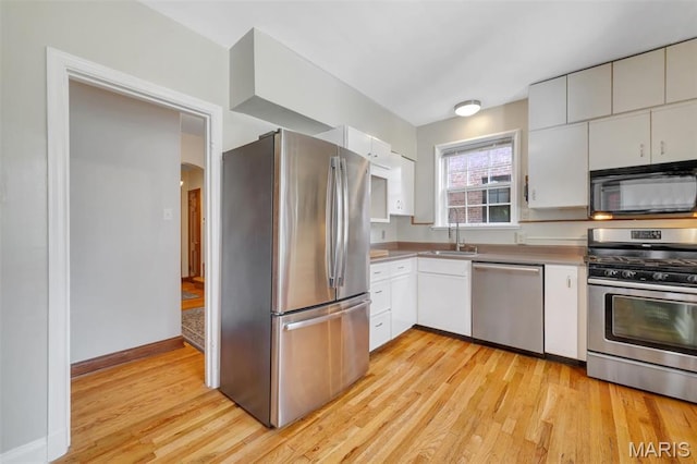 7423 Tulane Ave, Saint Louis, MO 63130 - kitchen featuring stainless steel appliances, light wood-style floors, arched walkways, and white cabinetry