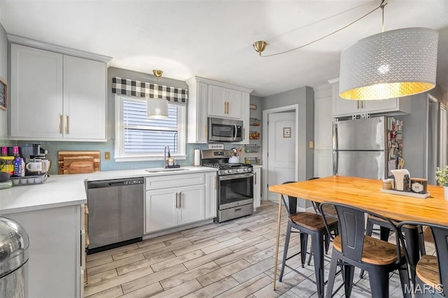 kitchen with appliances with stainless steel finishes, a sink, light countertops, light wood finished floors, and white cabinets