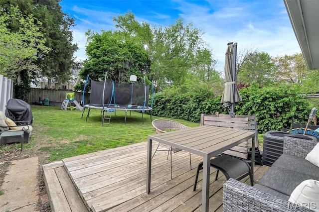 wooden terrace featuring a trampoline, outdoor dining space, and a playground