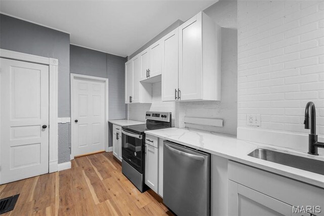 2148 Oregon Ave, Saint Louis, MO 63104 - kitchen featuring appliances with stainless steel finishes, a sink, light wood finished floors, white cabinetry, and tasteful backsplash