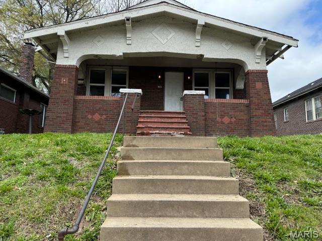 view of front of property with brick siding, a porch, stucco siding, and stairs