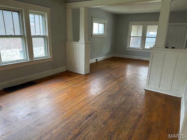 empty room featuring ornate columns, dark wood-type flooring, and baseboards