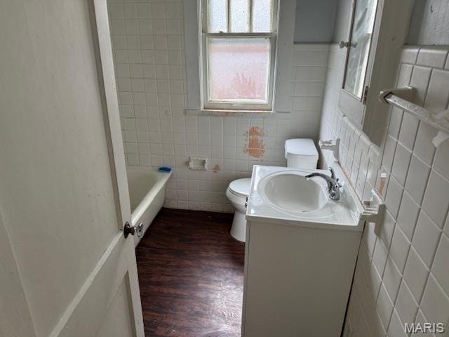 full bath with tile walls, toilet, wood finished floors, vanity, and a tub to relax in