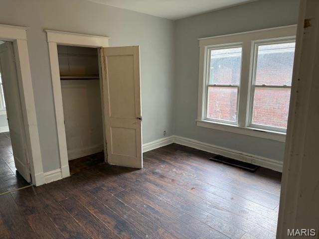 unfurnished bedroom with dark wood finished floors, baseboards, and a closet