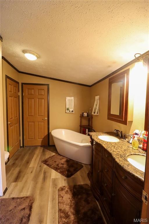 bathroom featuring crown molding, a textured ceiling, a soaking tub, wood finished floors, and double vanity