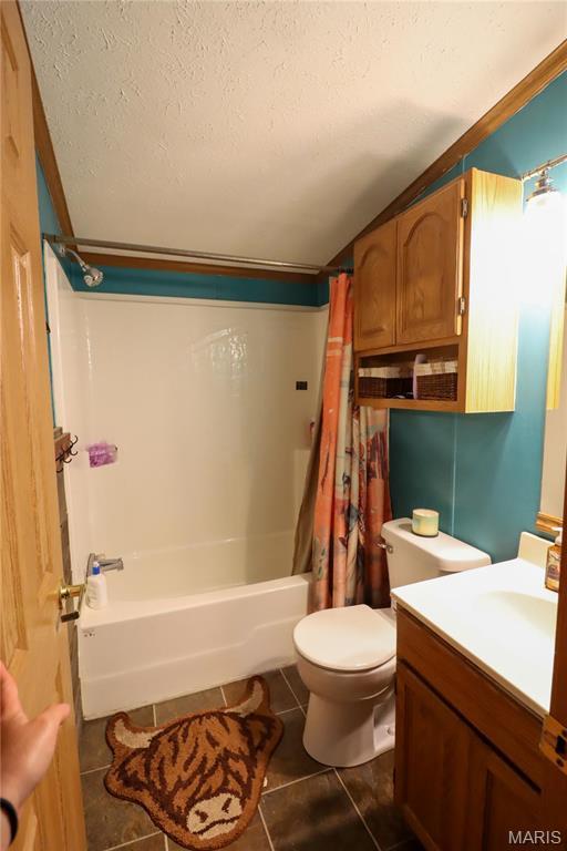 bathroom featuring tile patterned floors, a textured ceiling, toilet, shower / bath combo, and vanity