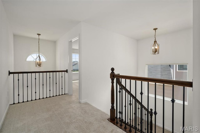 corridor featuring a chandelier, an upstairs landing, carpet, and baseboards