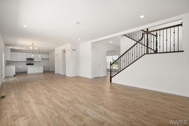 unfurnished living room featuring light wood-type flooring, baseboards, stairs, and recessed lighting