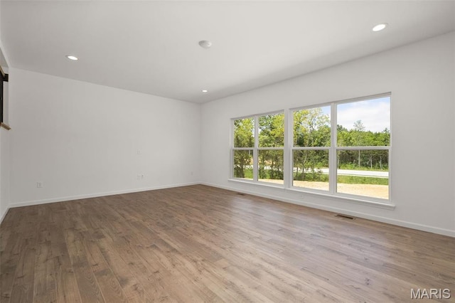 unfurnished room with plenty of natural light, wood finished floors, recessed lighting, and baseboards