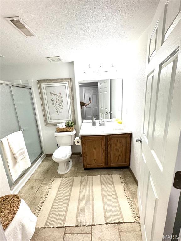 bathroom with a shower stall, toilet, vanity, a textured ceiling, and baseboards