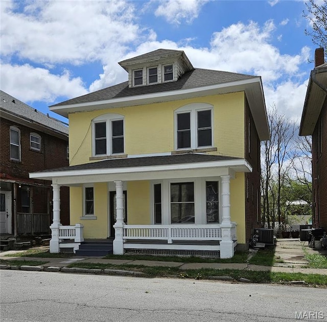 american foursquare style home with a porch, central AC unit, and roof with shingles