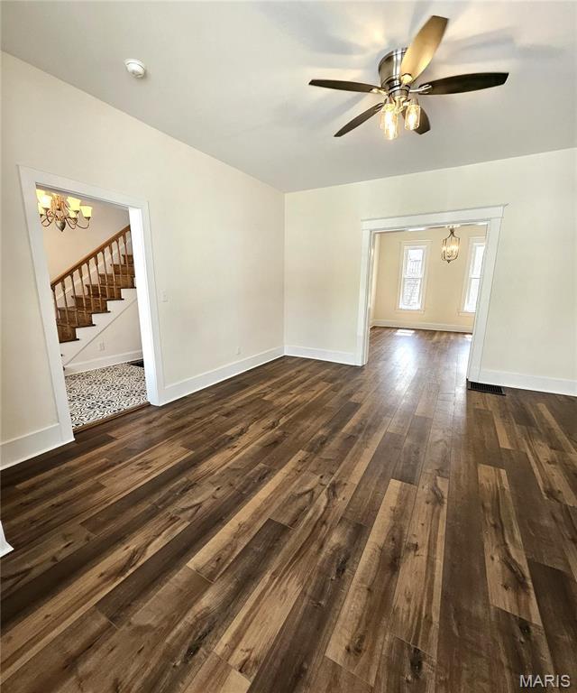 unfurnished living room featuring a chandelier, dark wood-type flooring, stairway, a ceiling fan, and baseboards