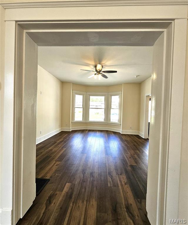 unfurnished room featuring dark wood finished floors, ceiling fan, and baseboards