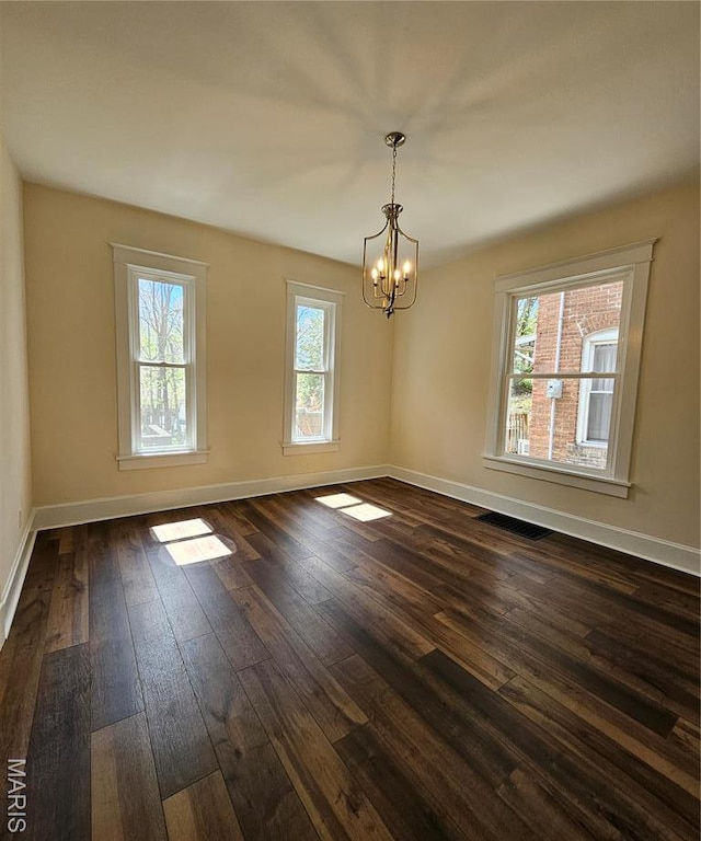 empty room featuring a chandelier, dark wood-style floors, and baseboards