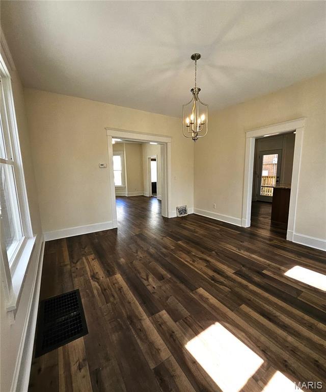 spare room featuring a chandelier, dark wood finished floors, and baseboards