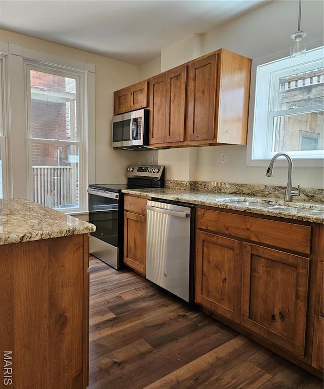 kitchen featuring appliances with stainless steel finishes, a sink, dark wood-style flooring, brown cabinetry, and light stone countertops