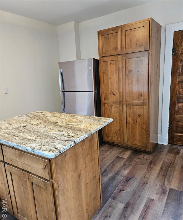 kitchen featuring dark wood finished floors, light stone counters, freestanding refrigerator, and brown cabinetry