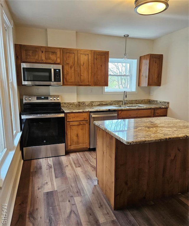 kitchen featuring appliances with stainless steel finishes, a sink, wood finished floors, and brown cabinets