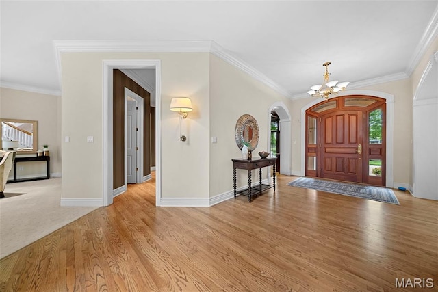 foyer entrance featuring a chandelier, arched walkways, light wood finished floors, baseboards, and crown molding