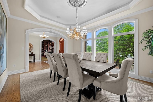 dining area featuring a chandelier, a tray ceiling, arched walkways, crown molding, and light wood-style flooring