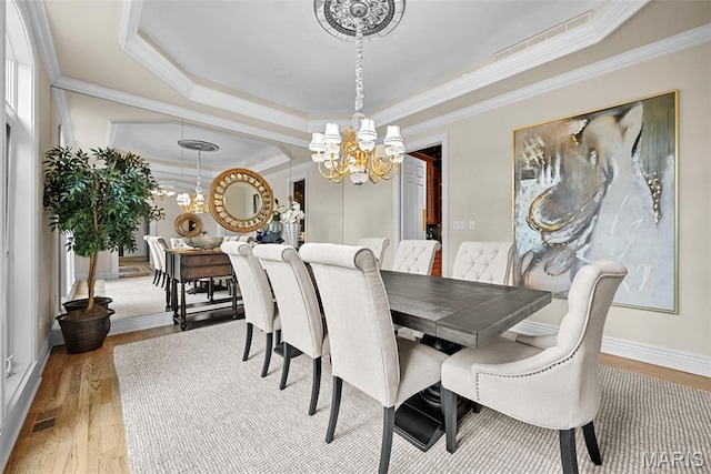 dining room featuring a chandelier, a tray ceiling, wood finished floors, ornamental molding, and baseboards