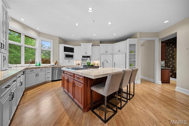 kitchen with appliances with stainless steel finishes, a kitchen breakfast bar, light wood-style floors, light stone countertops, and recessed lighting