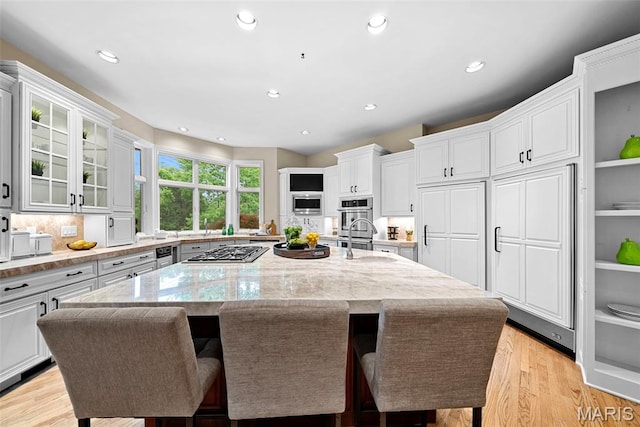 kitchen featuring stainless steel gas stovetop, a large island with sink, white cabinets, light stone countertops, and recessed lighting