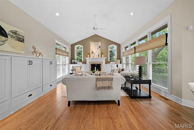 living area featuring a ceiling fan, healthy amount of natural light, light wood-style flooring, a fireplace, and vaulted ceiling