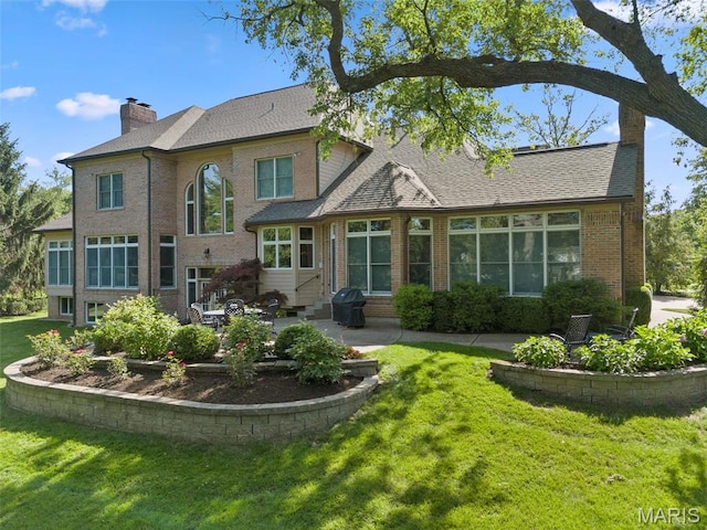 back of house with a chimney, a patio area, a lawn, entry steps, and brick siding