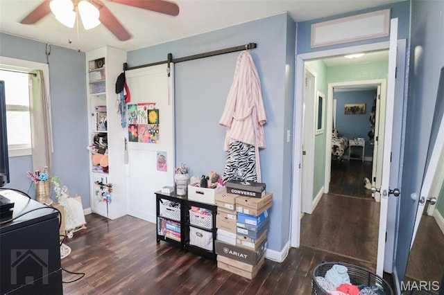bedroom featuring dark wood-style floors, baseboards, a barn door, and ceiling fan