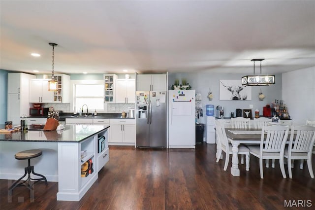kitchen featuring stainless steel fridge, freestanding refrigerator, dark countertops, white cabinetry, and glass insert cabinets