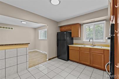 1605 Koch Dr, Florissant, MO 63033 - kitchen with freestanding refrigerator, light countertops, a sink, brown cabinets, and healthy amount of natural light