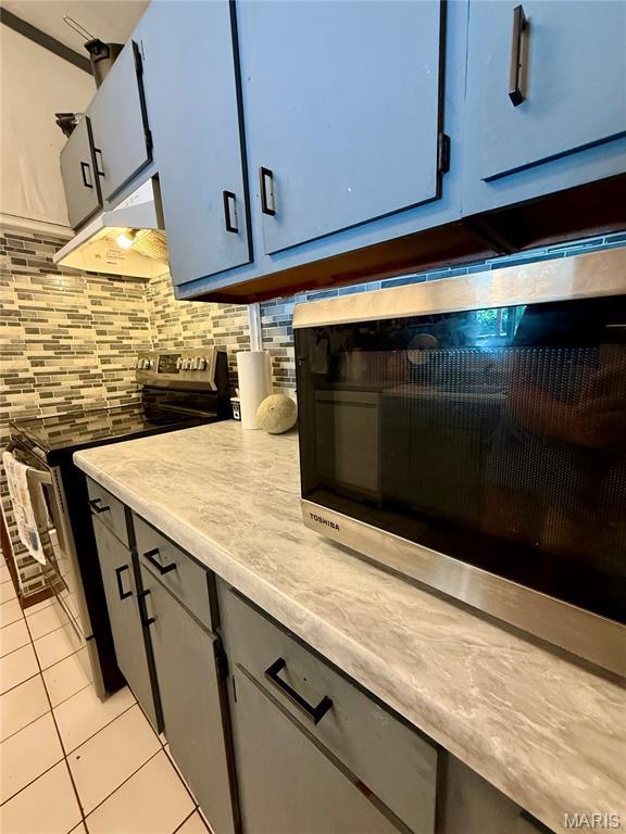56 Berger Rd, Middletown, MO 63359 - kitchen with appliances with stainless steel finishes, light tile patterned floors, under cabinet range hood, backsplash, and light countertops