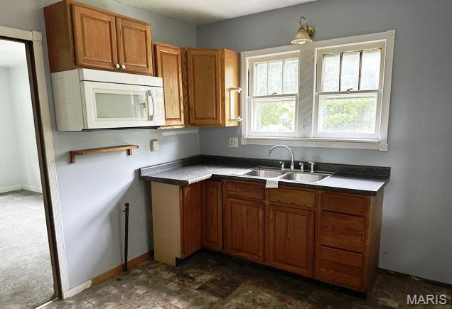9909 Baltimore St, Belleville, IL 62223 - kitchen with white microwave, a sink, brown cabinets, and baseboards