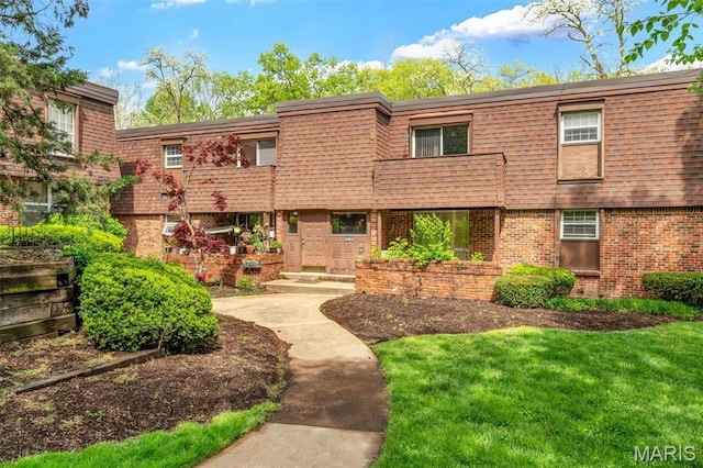 view of front of property featuring brick siding, a balcony, mansard roof, and a front lawn