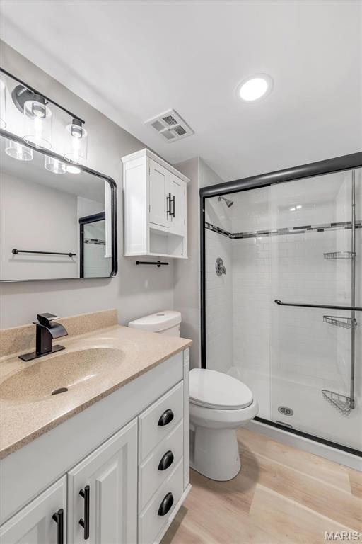 bathroom featuring wood finished floors, a stall shower, toilet, and vanity