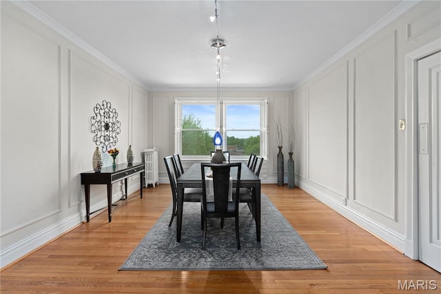 dining room with a decorative wall, crown molding, light wood-style flooring, and rail lighting