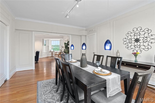 dining room featuring a decorative wall, light wood-style floors, crown molding, and track lighting