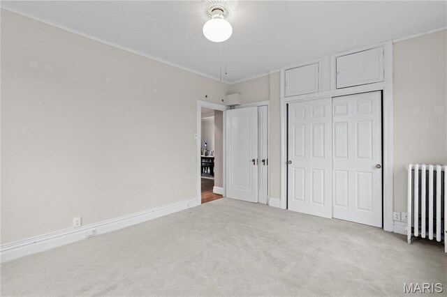 unfurnished bedroom with radiator, carpet flooring, multiple closets, crown molding, and baseboards