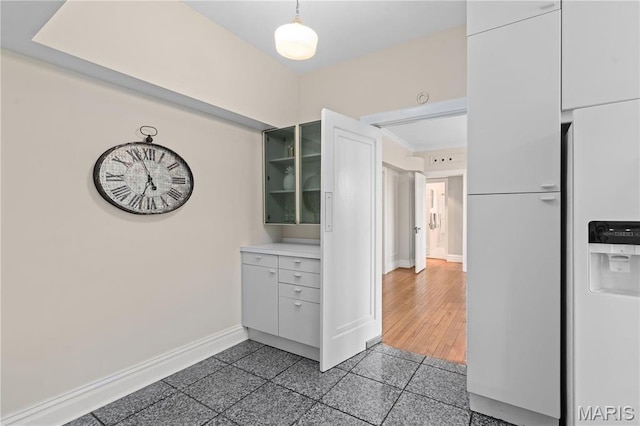kitchen with baseboards, light countertops, granite floors, glass insert cabinets, and decorative light fixtures