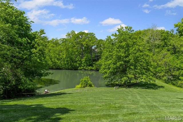 view of green lawn featuring a water view and a forest view