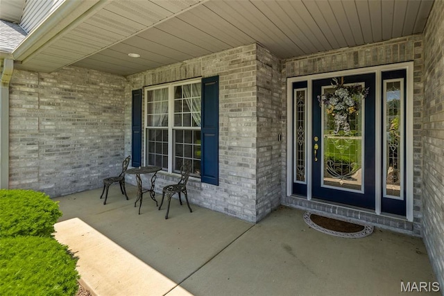 view of exterior entry featuring covered porch and brick siding