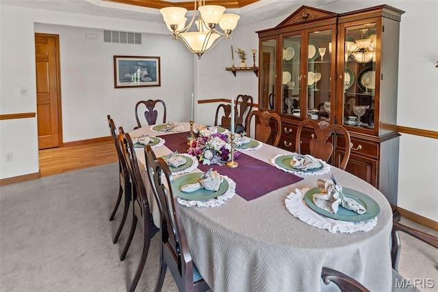 carpeted dining space featuring a chandelier, baseboards, and a raised ceiling